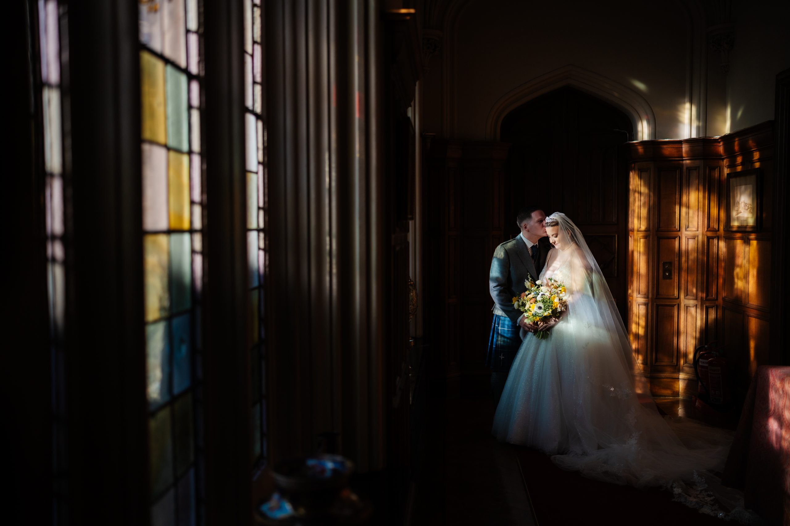 Bride and Groom standing together, bathed in light beaming through stained glass windows