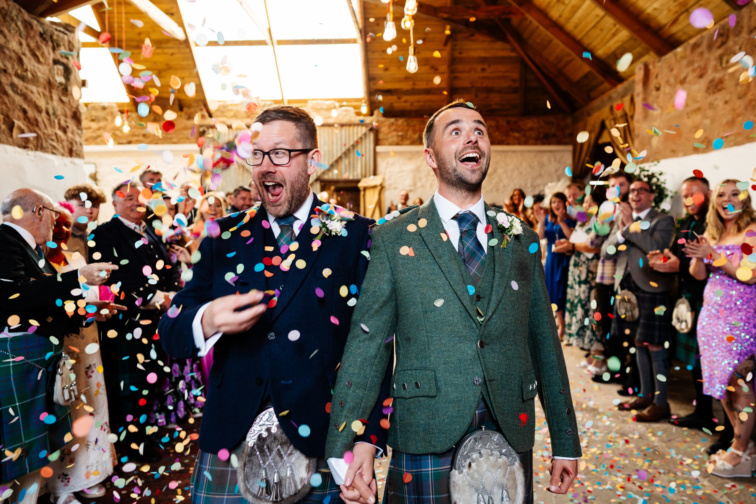 Two young men celebrate their vows by being surrounded by colourful confetti, thrown by their loved ones
